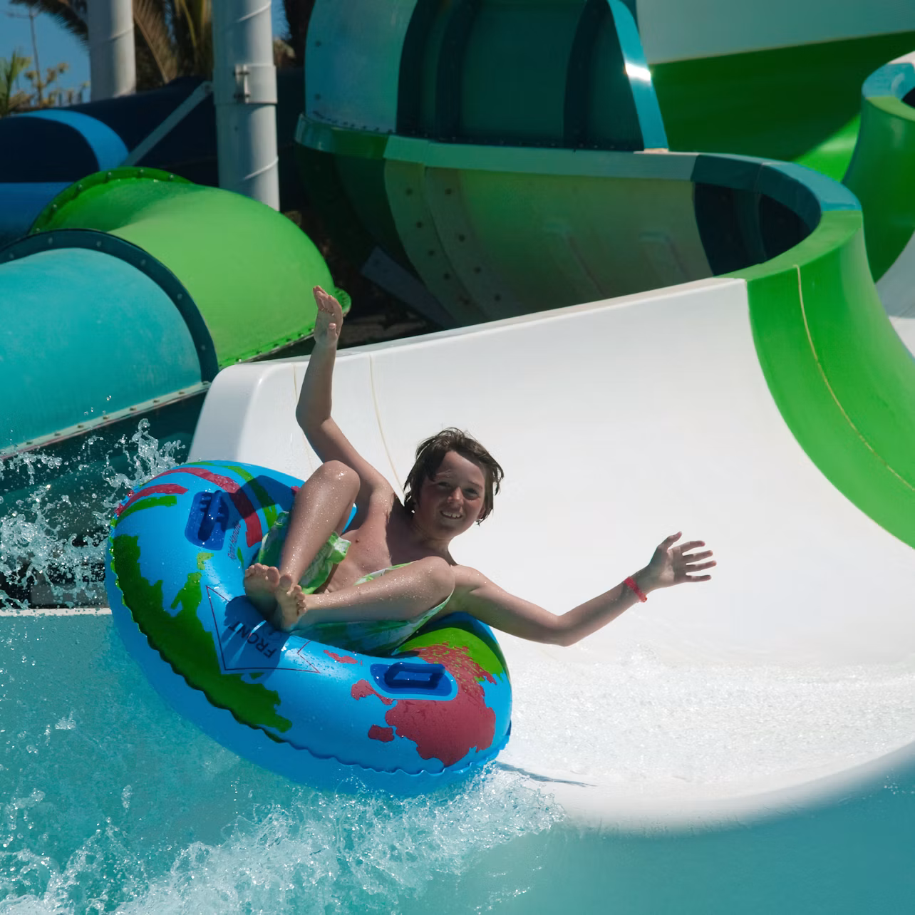A person sliding down a water slide on a colorful inflatable tube, with a joyful expression and raised arms.