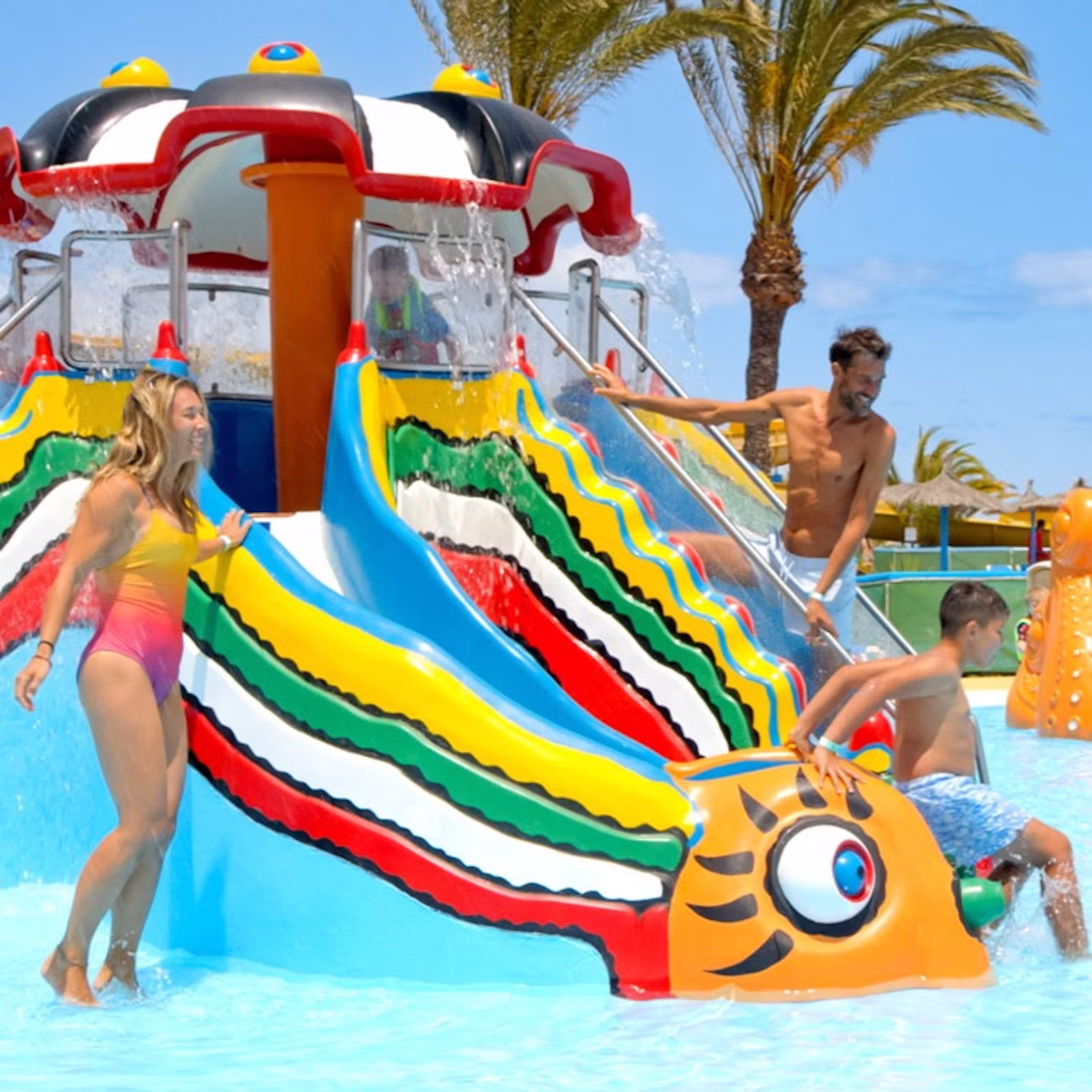 Children and adults playing on a colorful water slide shaped like a caterpillar in a sunny outdoor water park.