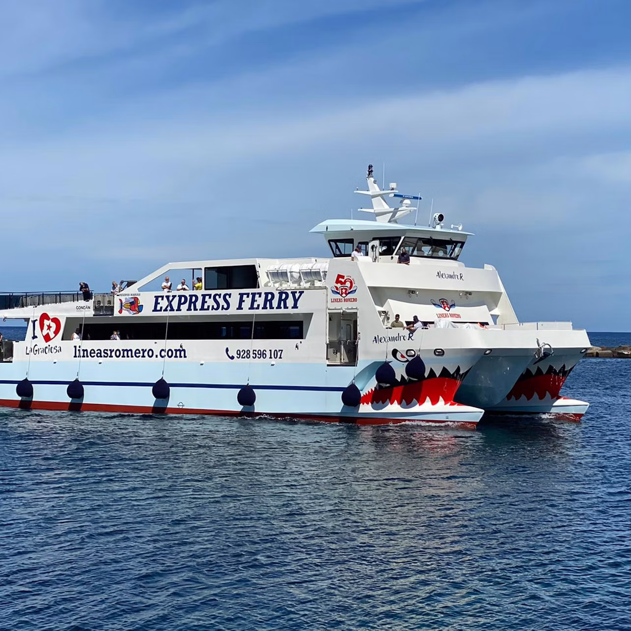 White ferry with "Express Ferry" and shark mouth design on the front, sailing on a calm sea under a clear blue sky.