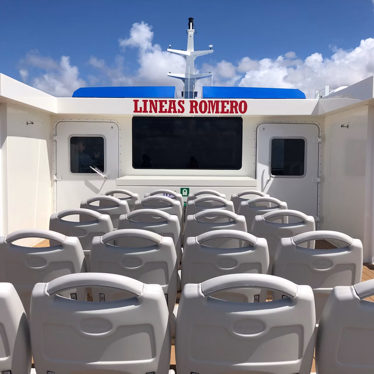 Rows of white seats on a ferry deck with "LINEAS ROMERO" signage, against a blue sky with scattered clouds.