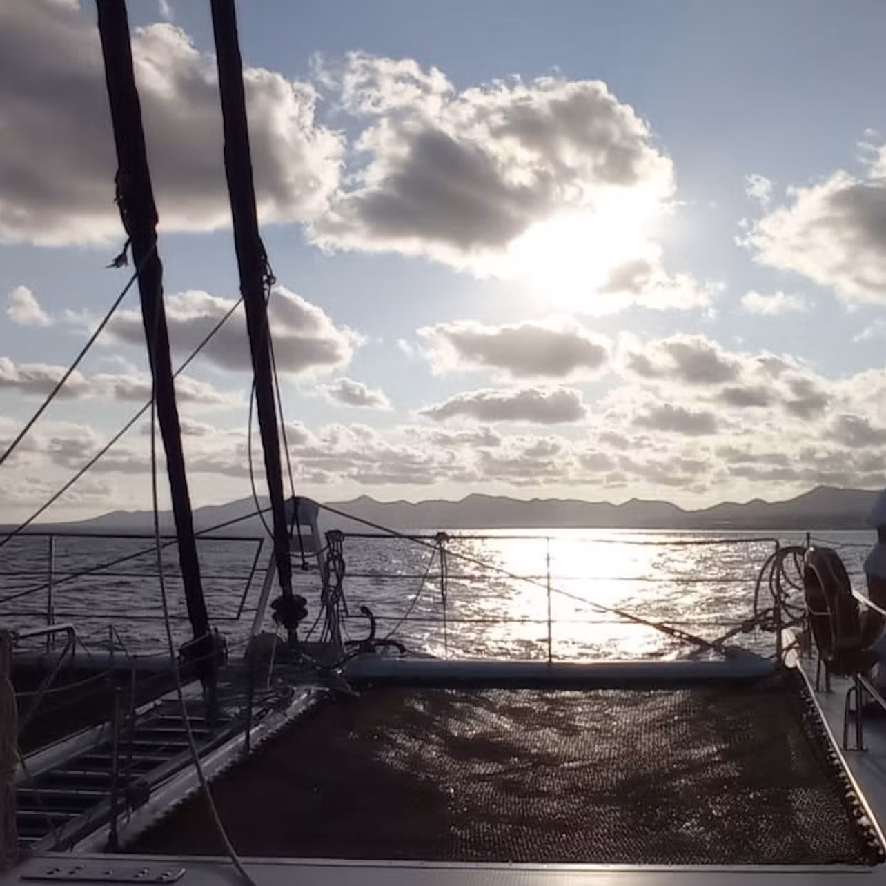 The deck of a sailboat at sunset with the sea and distant mountains in the background.