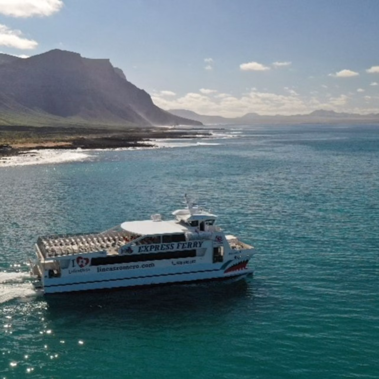 A white ferry boat labeled "EXPRESS FERRY" sails near a coastal mountain range under a partly cloudy sky.