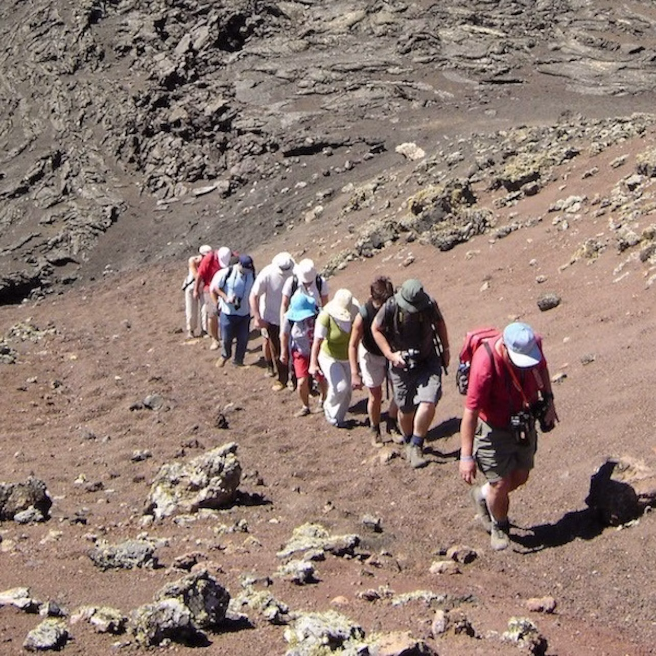 A group of hikers walking uphill on a rocky, barren terrain. The sky is not visible.