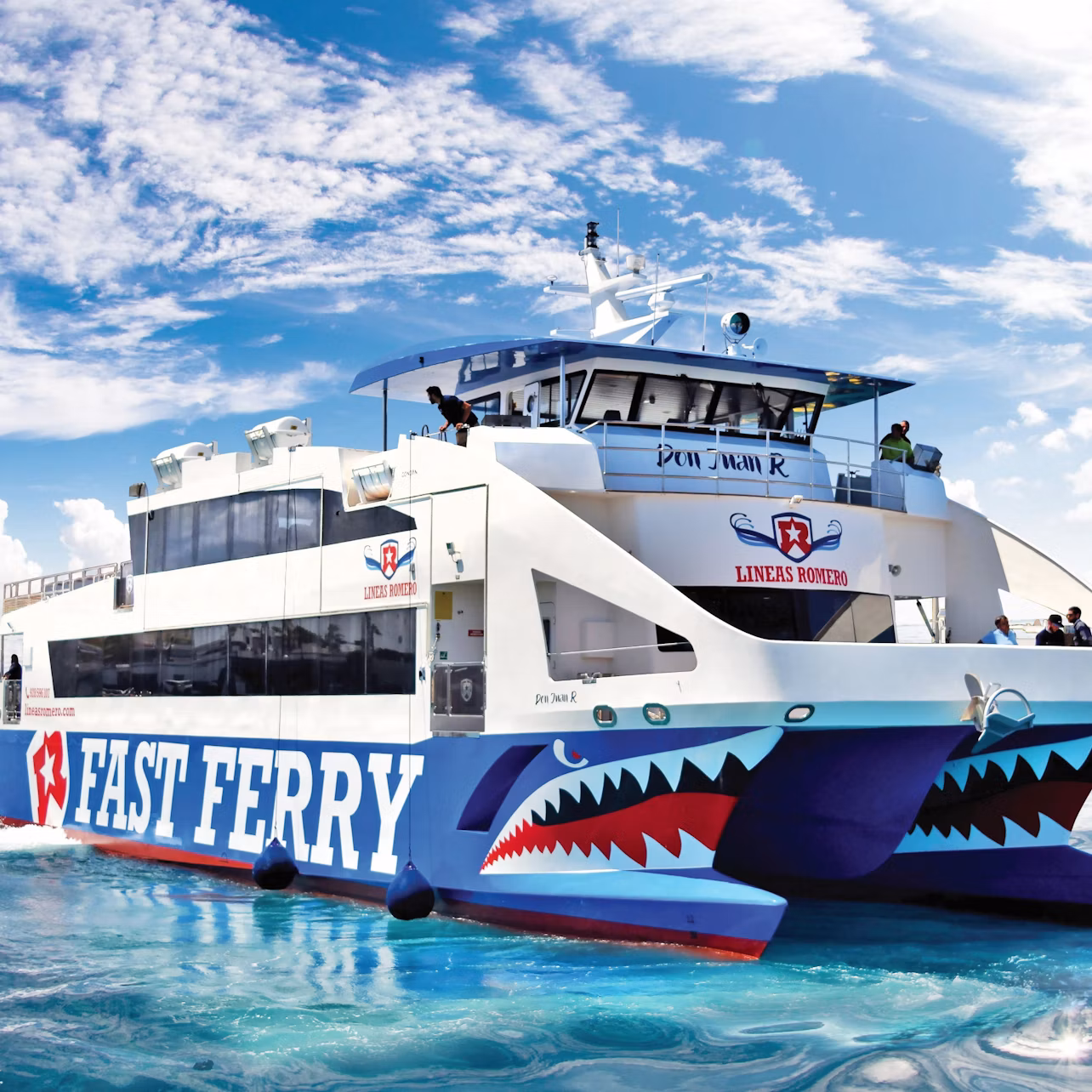 A white ferry with "FAST FERRY" and shark mouth designs on the hull on a clear, sunny day.