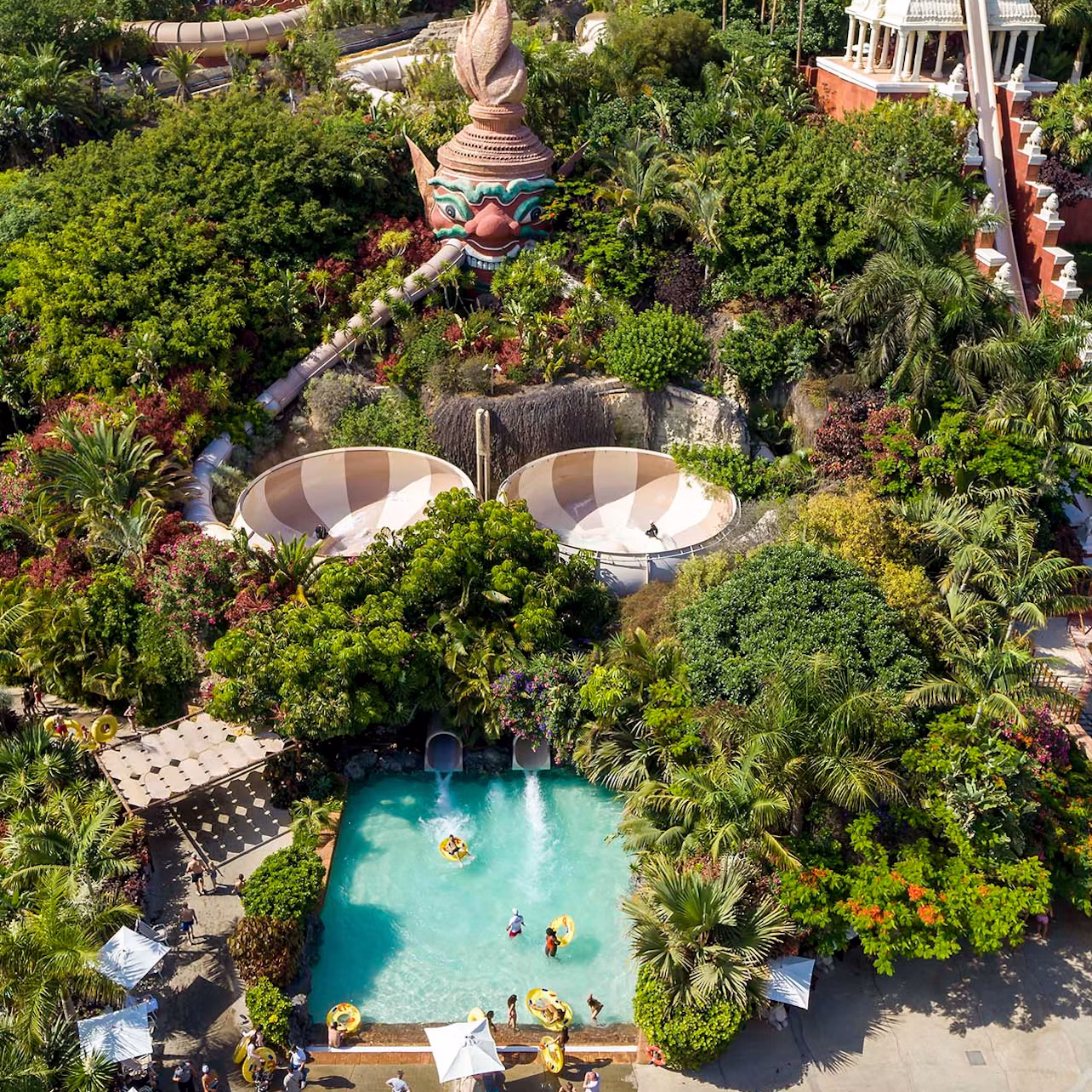 Aerial view of a water park with slides, pool, greenery, and people enjoying various recreational activities.