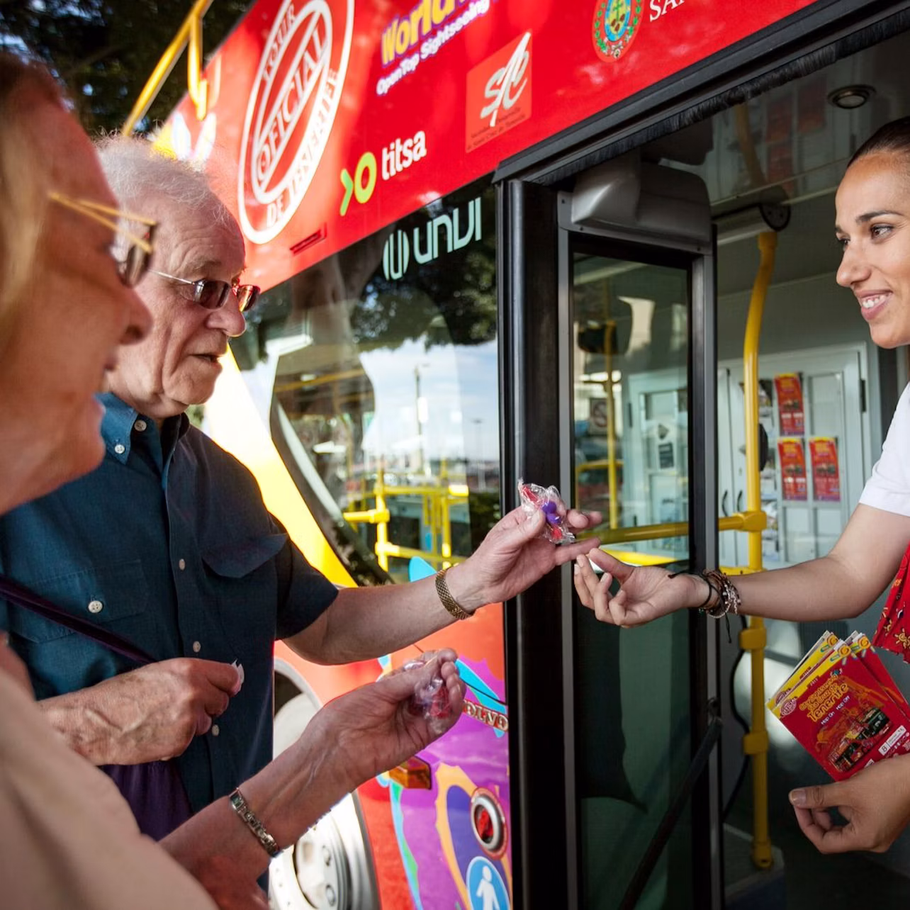 A uniformed woman stands in a bus entrance, handing an item to a person's outstretched hand.