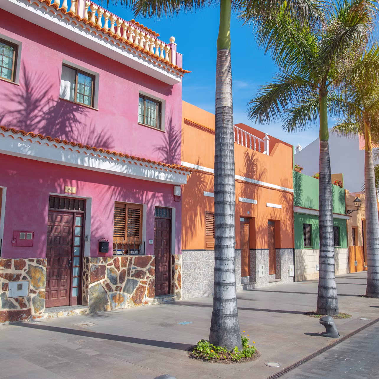 Colorful buildings with a pink and orange facade, palm trees lining the street, under a clear blue sky.
