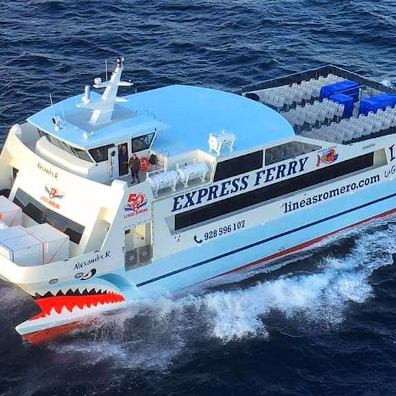 A white ferry named "Alexandre R" from "lineasromero.com" traveling through blue ocean water, with seating visible on the deck.