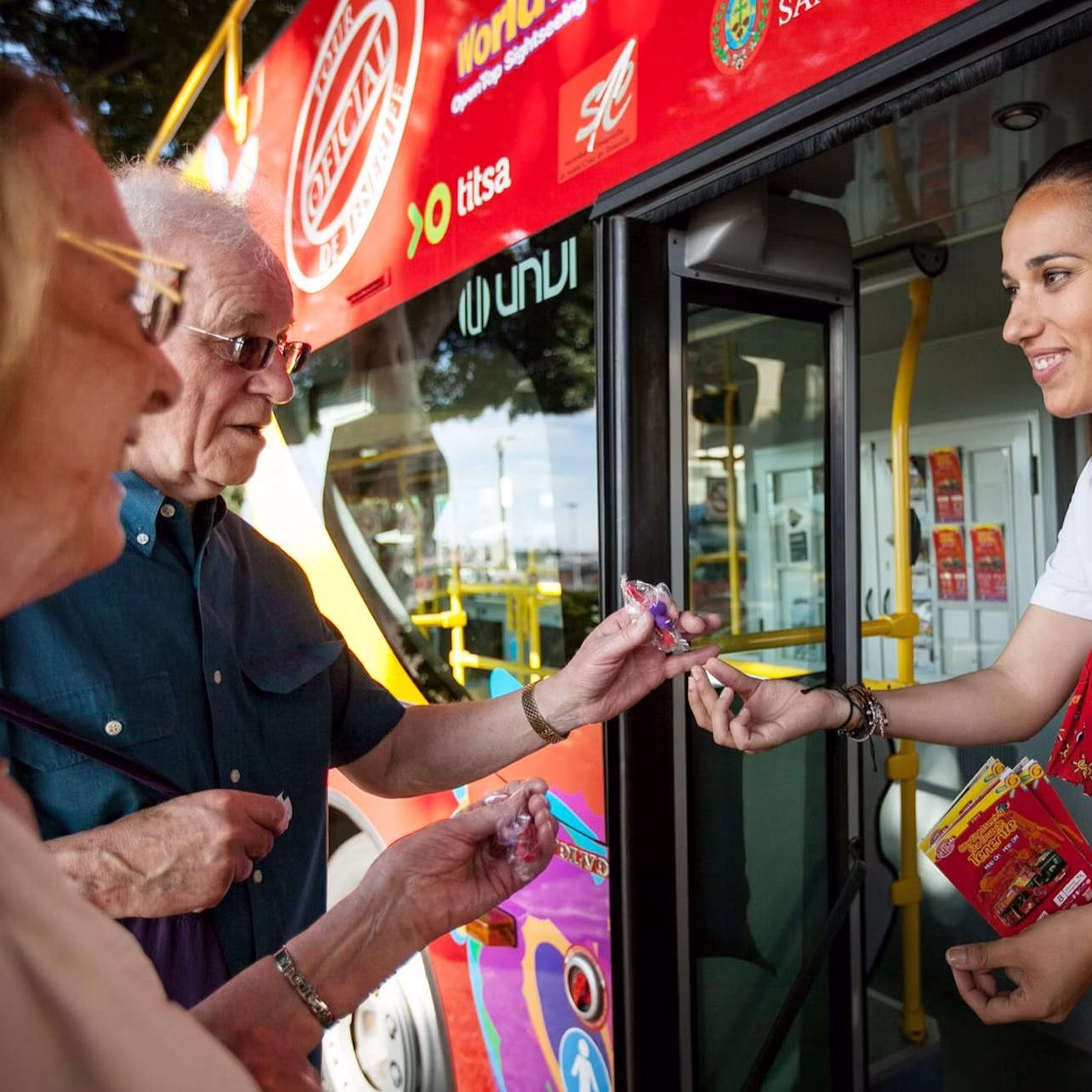 A uniformed woman stands in a bus entrance, handing an item to a person's outstretched hand.