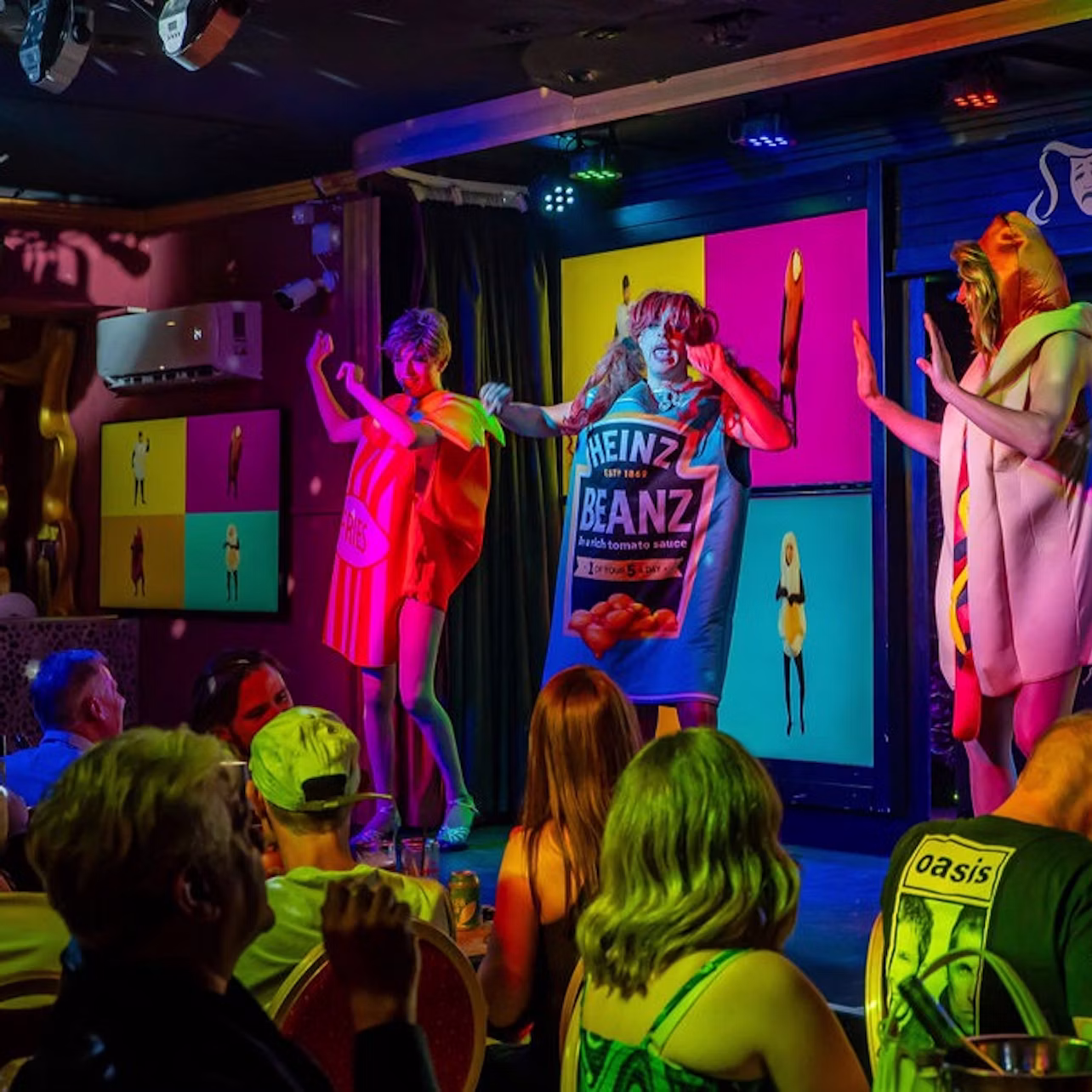 Performers in costume resembling food items on a colorful stage, with an audience seated in the foreground.