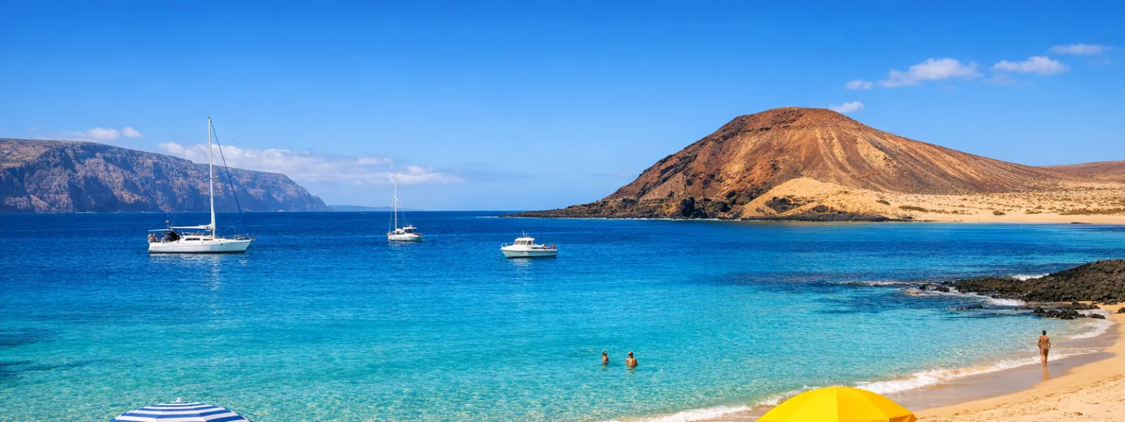 Spiaggia soleggiata a La Graciosa con acqua turchese, sabbia chiara e colline vulcaniche