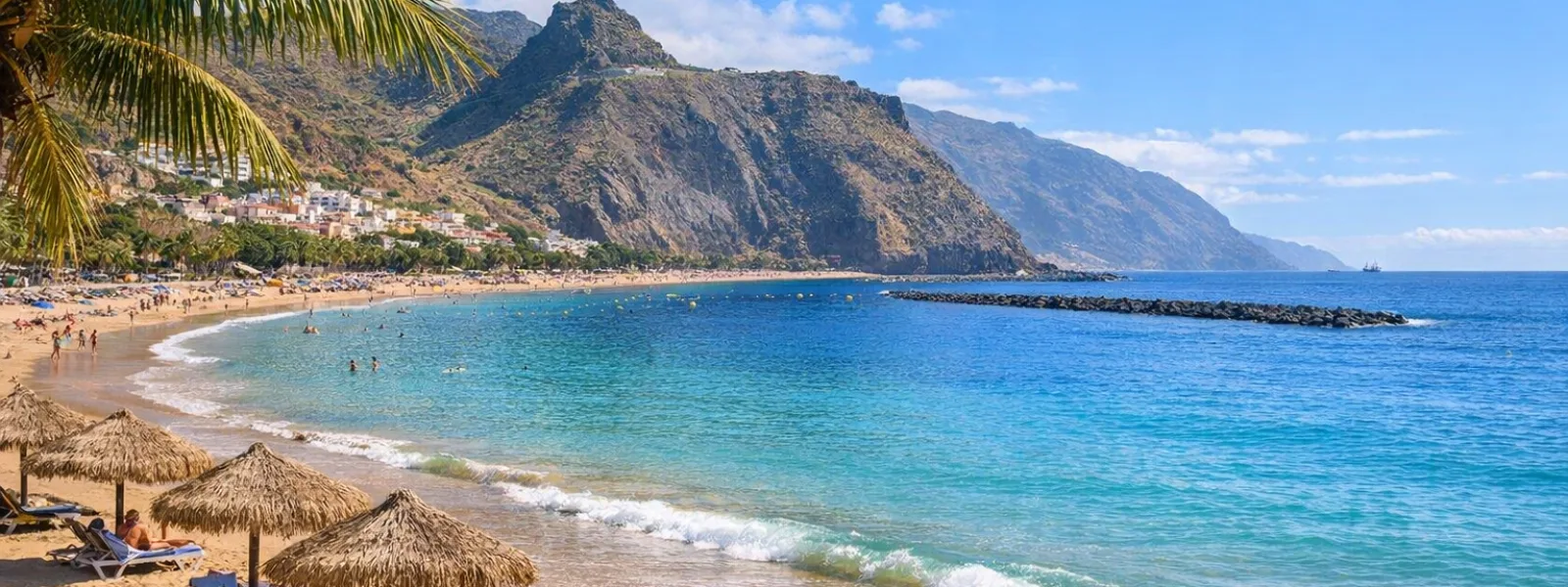 Spiaggia soleggiata a Tenerife con sabbia dorata, acqua turchese e sfondo montuoso