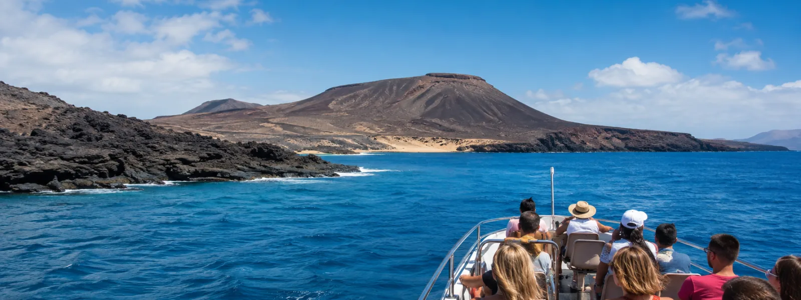 Travellers on a boat excursion approaching a volcanic Canary Islands coastline