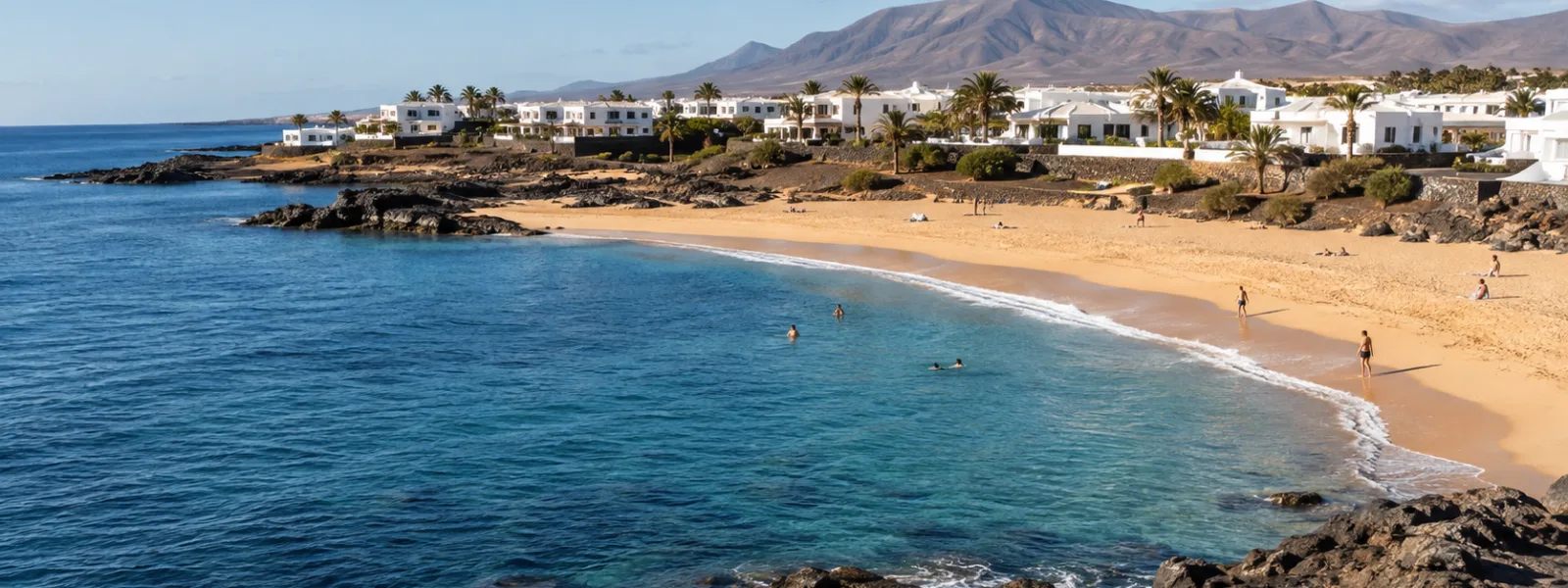 Spiaggia soleggiata delle Isole Canarie con rocce vulcaniche e edifici di resort imbiancati a calce a settembre