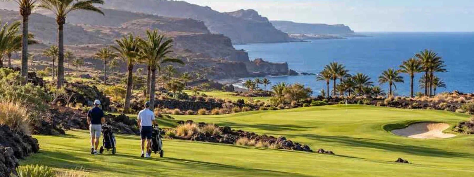 Golfers walking beside a green among volcanic hills and palms in southern Gran Canaria