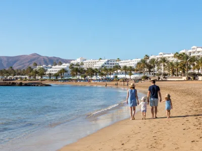 Family walking on Los Pocillos beach in Puerto del Carmen, Lanzarote, near low-rise resort hotels