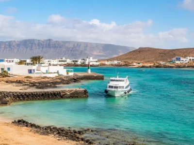 Ferry arriving at Caleta de Sebo on La Graciosa with turquoise water and Lanzarote cliffs
