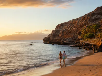 Couple walking on a quiet Tenerife beach at sunset with volcanic cliffs and the Atlantic Ocean