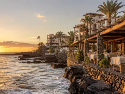 Golden-hour view of La Caleta in Tenerife with seafront restaurant terraces and upscale resort hotels