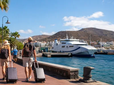 Travellers with luggage at Los Cristianos harbour in Tenerife near an inter-island ferry
