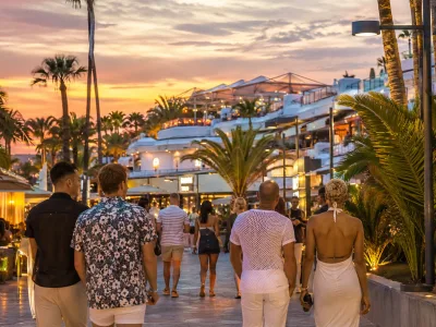 Adults walking near palm-lined hotels and nightlife by the Yumbo Centre in Playa del Ingles Gran Canaria