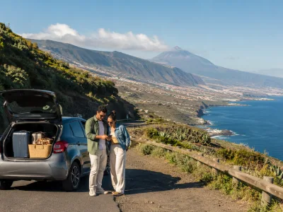 Travellers checking a map beside a rental car on a scenic Tenerife coastal road