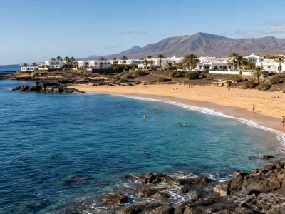 Sunny Canary Islands beach with volcanic rocks and whitewashed resort buildings in September