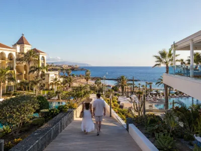 Couple walking between a colonial-style luxury resort and a modern adults-only hotel on the Costa Adeje coast in Tenerife