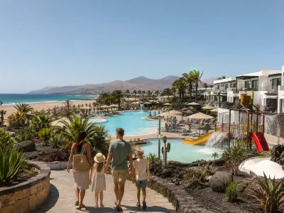 Family walking toward a beachfront resort pool and splash area at Playa de los Pocillos, Lanzarote