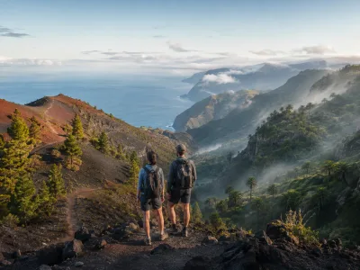 Hikers overlooking volcanic slopes and a misty green ravine representing La Palma and La Gomera