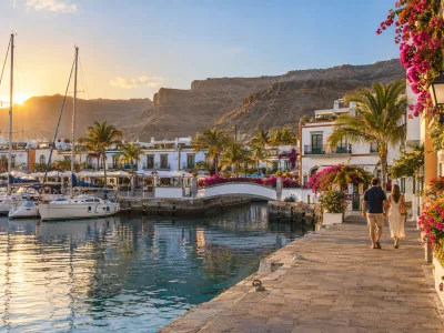 Couple walking beside the marina and whitewashed buildings of Puerto de Mogán at sunset