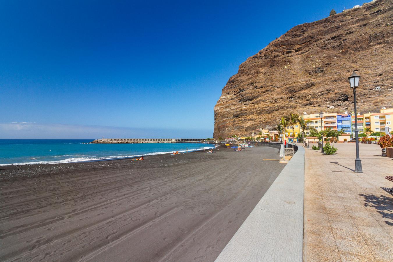 Beach in La Palma with black sand, promenade and volcanic cliffs
