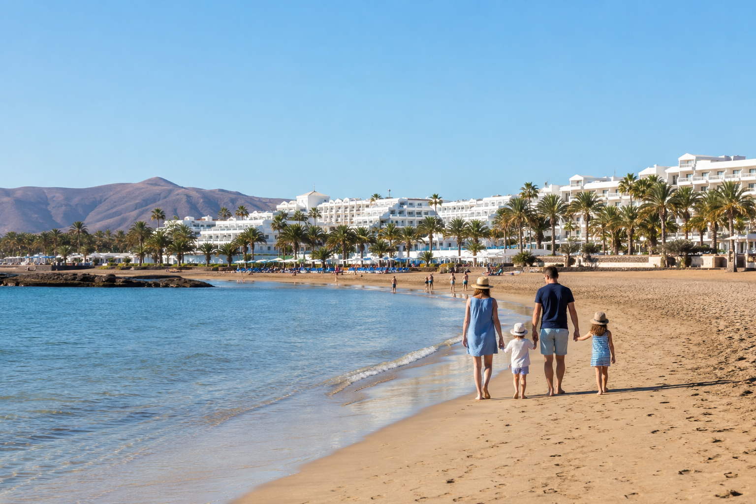 Family walking on Los Pocillos beach in Puerto del Carmen, Lanzarote, near low-rise resort hotels